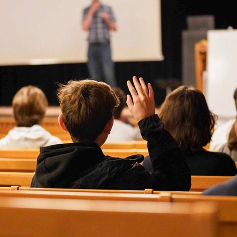 A lecture in front of a school class where one of the children raises a hand.