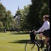 castle in the background and a young woman comes cycling in the foreground