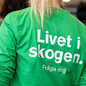 Närbild på ryggen på en person som har en grön tröja där det står "Livet i skogen. Fråga mig!" på ryggen. Foto.