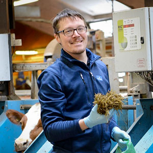 A man stands in a barn holding a fistful of hay. Photo.
