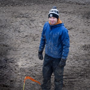 A man in a blue jacket is standing on a muddy field. Photo. 