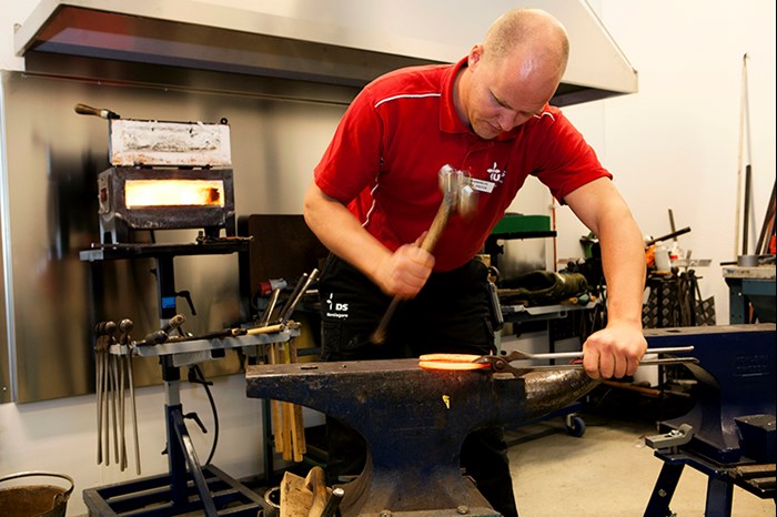 En person hamrar på en glödande hästsko på ett städ. Foto