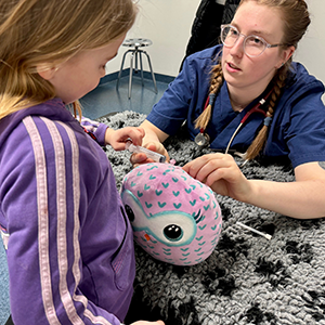 En veterinärstudent undersöker ett gosedjur, intill står ett barn och tittar på.