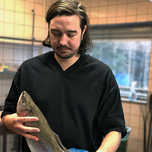 A young man standing at a table holding a fish. Photo.