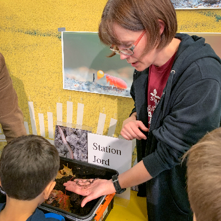 En kvinna visar daggmaskar i jord för barn. Foto.