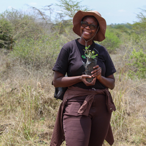 A smiling woman in a sun hat is holding a plant outdoors. Photo.