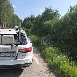 En bil vid en vägkant på mindre väg, med en kamera monterad på bakrutan. Foto,