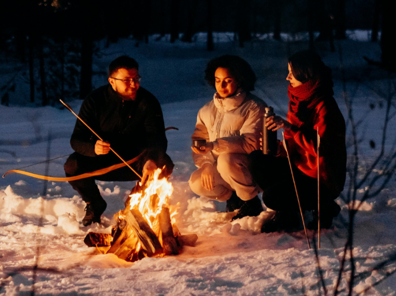 Tre personer sitter runt en eld