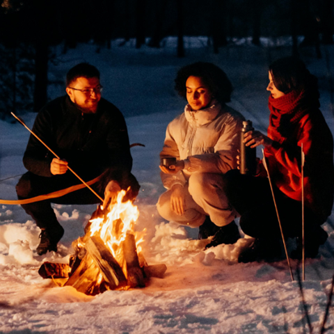 Tre personer sitter runt en eld