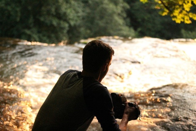 Man med kamera vid ett vattendrag.
