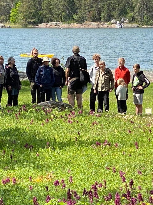 En guide står framför en grupp. I bakgrunden syns vatten.