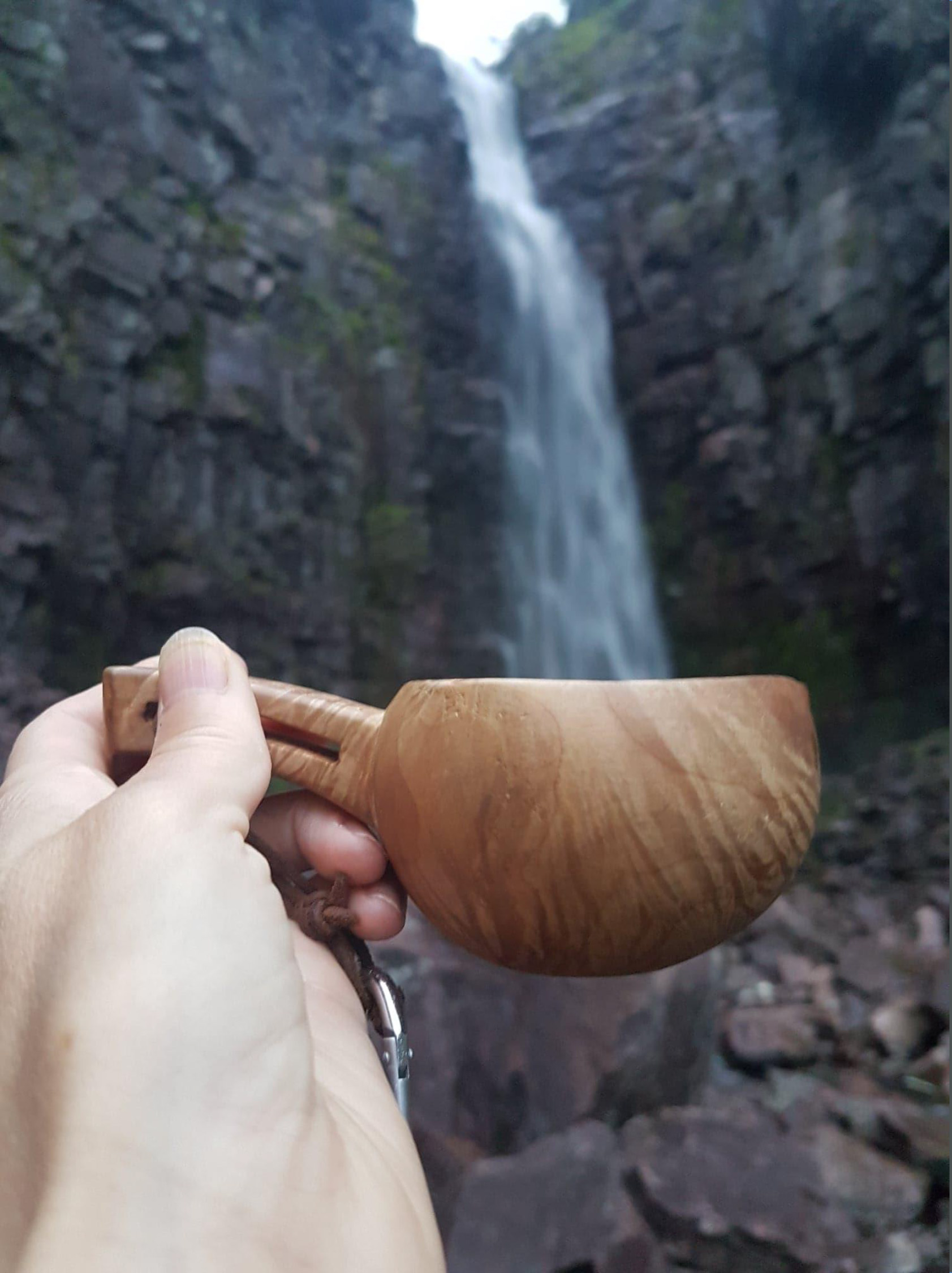 En träkåsa hålls framför vattenfallet Njupeskär