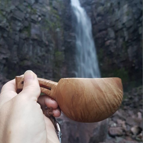 En träkåsa hålls framför vattenfallet Njupeskär