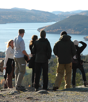 En grupp människor utomhus. I bakgrunden vatten och berg. Foto.