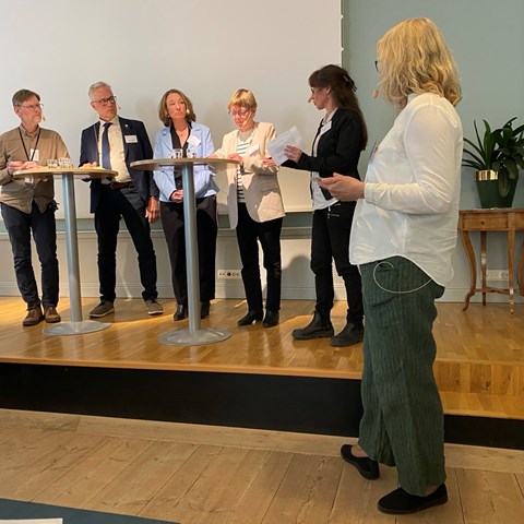 En grupp människor står uppradade och diskuterar vid några ståbord. Foto.