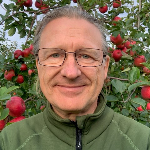 Porträttbild av Kimmo framför ett äppelträd fullt av röda äpplen.
