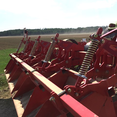 Bakändan av en traktor, ett rött redskap sitter på, stora fält i bakgrunden.