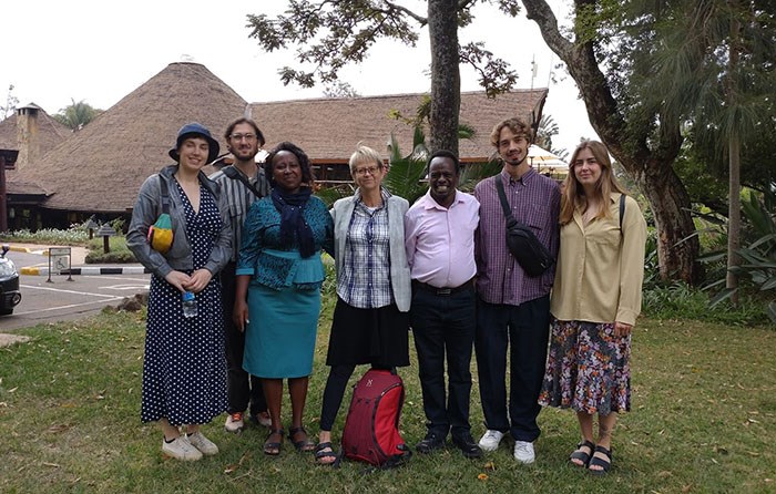 A group of people standing on a lawn, in the background grass thatched roofs. Photo.