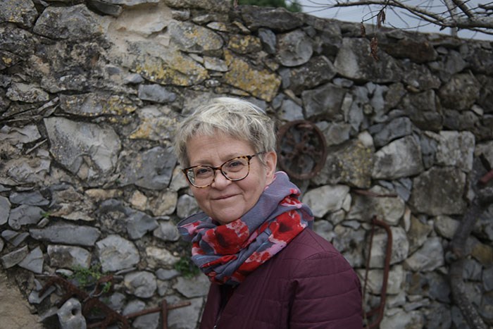 A woman smiling in front of a stone wall. Photo.