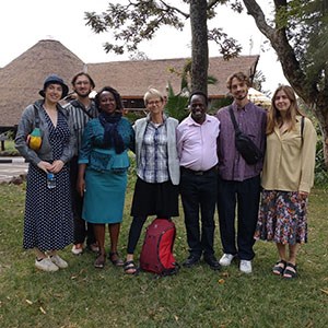 En grupp människor som står på en gräsmatta framför hus med gräsklädda tak. Foto.