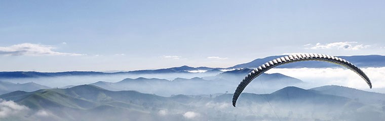 Skärmflygare över moln och berg. Foto.
