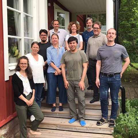 Gruppfoto. Tio glada personer står på en trappa till ett rött hus.