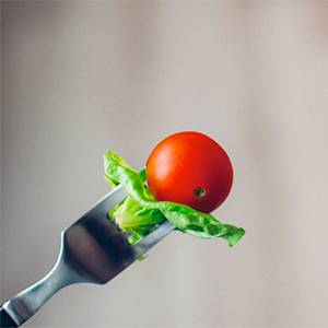En gaffel med tomat och sallad på mot grå bakgrund. Foto.