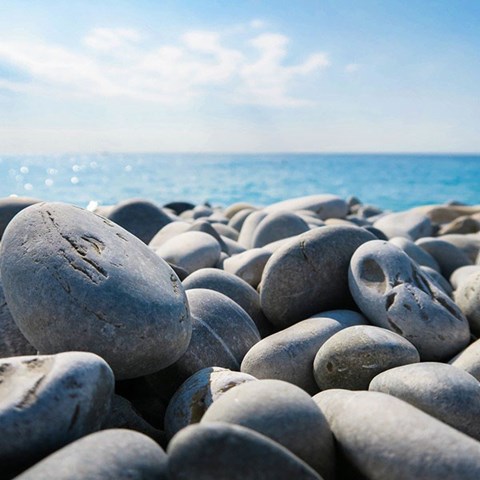 Gråa rundade stenar på en strand, i bakgrunden hav och horisont