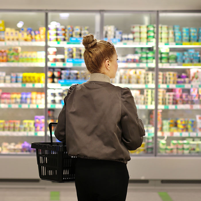 En kvinna sedd bakifrån står med en kundkorg i en mataffär. Foto.