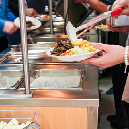 People serving themselves food in a line. Photo.