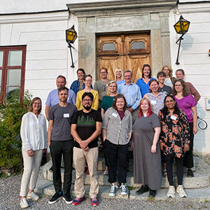 Ett 20-tal kvinnor och män står på en stentrappa framför en herrgård. Foto.