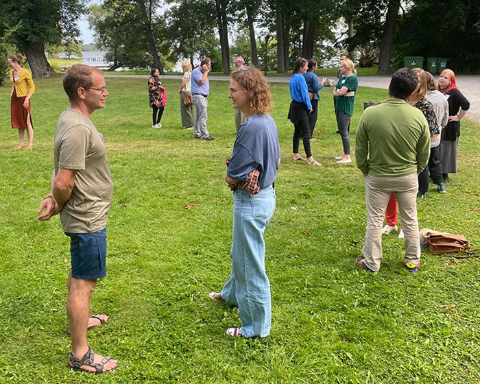 About 20 people spread out on a lawn, talking to each other in pairs. Photo.