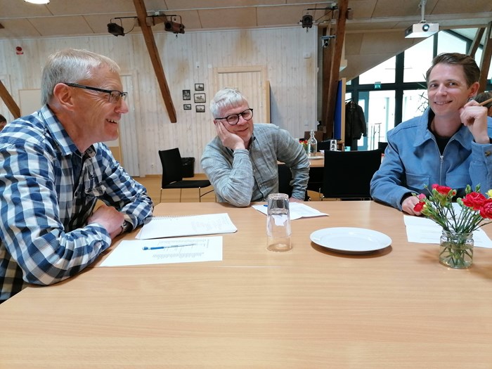 Tre personer sitter runt ett bord och diskuterar leende