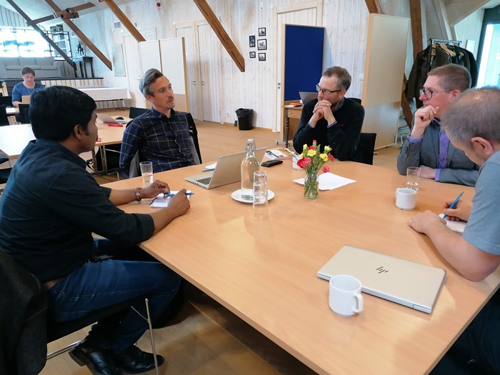 Fem personer sitter runt ett bord på en konferens och diskuterar
