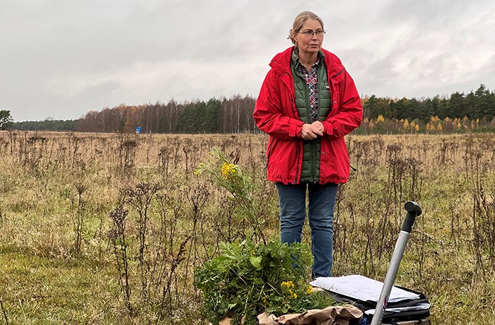 En kvinna står på et fält. Framför sig har hon växten stånds