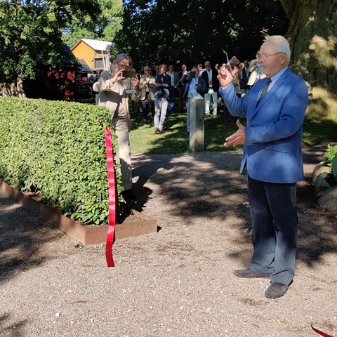 Invigning av klonarkivet vid DBW. Sven-Erik Lindström, ordförande i trädgårdsstyrelsen vid DBW, har just klippt av ett rött band in till klonarkivet och håller saxen i luften. I bakgrunden ses en skara finklädda människor som applåderar.