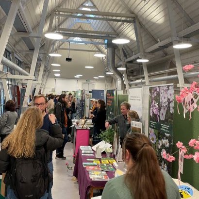 Utställare på Landskapsingenjörsdagen 2023. På Loftet i Alnarpsgården har anordnats en utställning och golvet är täckt av informationsbord, rollups och informationsmaterial. Besökare minglar runt i utställningen och pratar med utställare. 