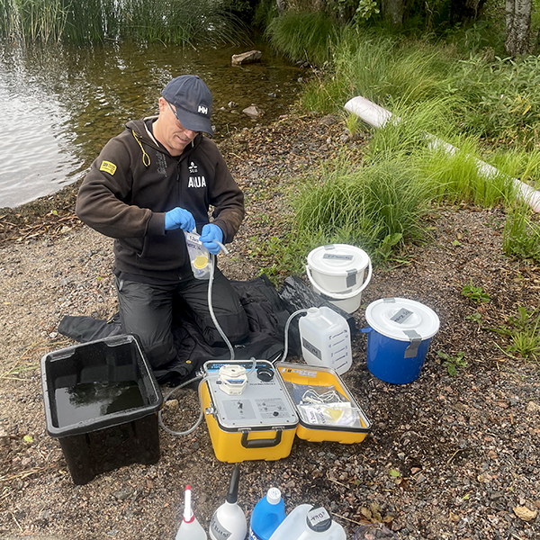 Person som sitter på strandkant och mäter upp vatten i plastdunkar