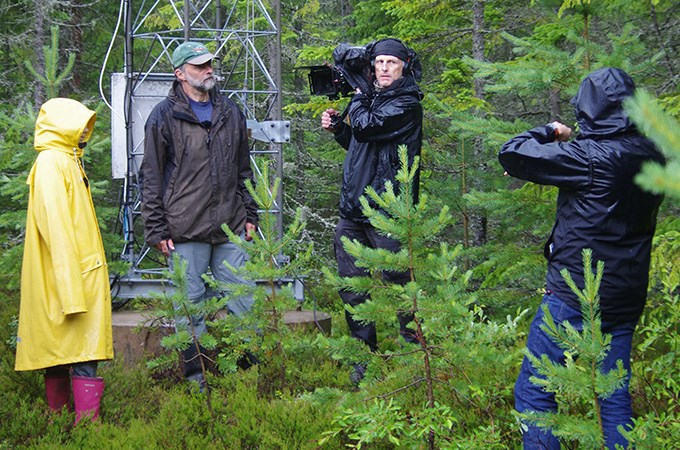 Man med stor filmkamera filmar några personer i skogen.
