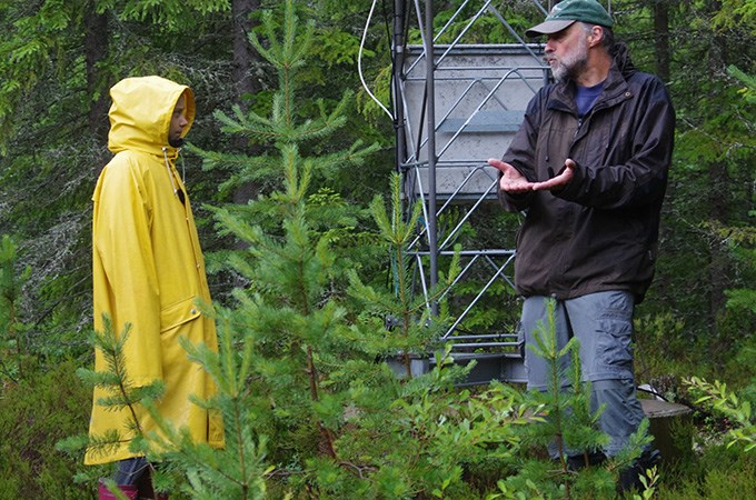 Kvinna i gul regnrock och man i mörk jacka diskuterar i skogen.
