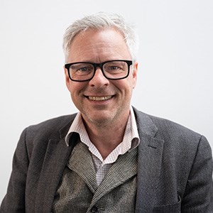 Man med grått hår, glasögon och klädd i kavaj