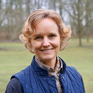 Kvinna med kort lockigt hår, klädd i blå jacka