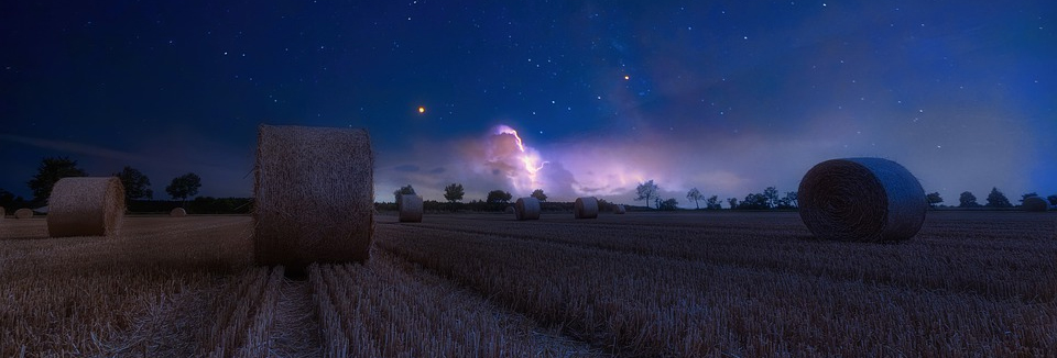 Höbalar på ett fält under en stjärnhimmel, foto.
