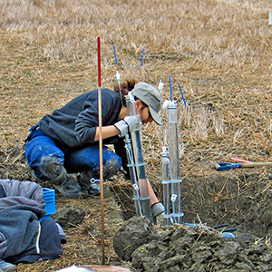 En kvinna vid ett hål på ett fält. Foto.