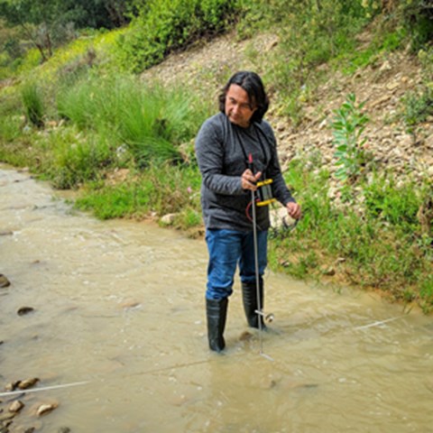 A man is standing in a river holding a measuring tool. Photo. 