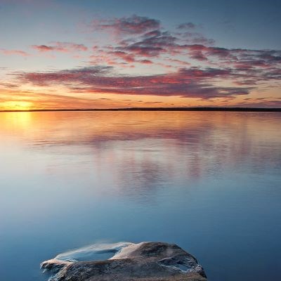 sjö i solnedgång. Sten i förgrunden.