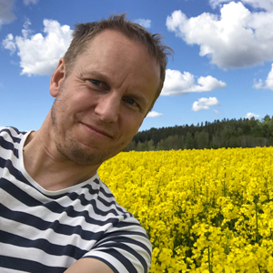 En man utomhus framför ett rapsfält. Foto.