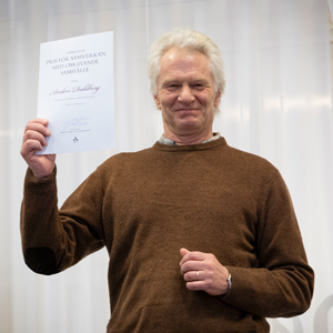 En glad man håller upp ett diplom. Foto.