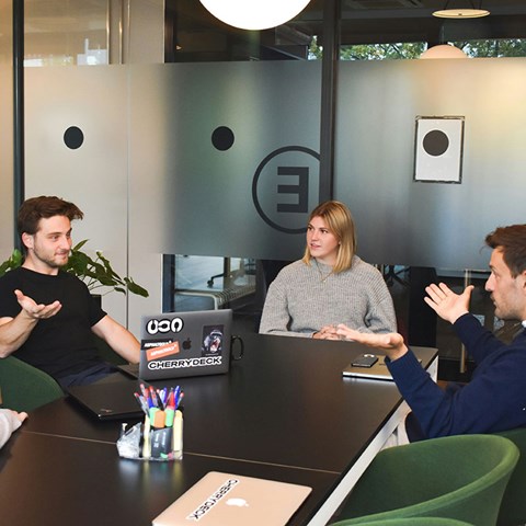 Tre personer sitter runt ett bord och diskuterar. Foto.