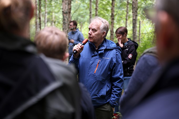 Person talking to people among birch trees. Photo.